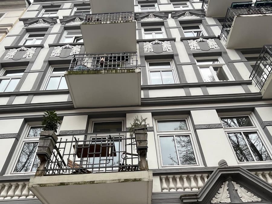 Weiß-graue Altbaufassade mit schmiedeeisernen Balkonen und Stuckgiebel über dem Eingang