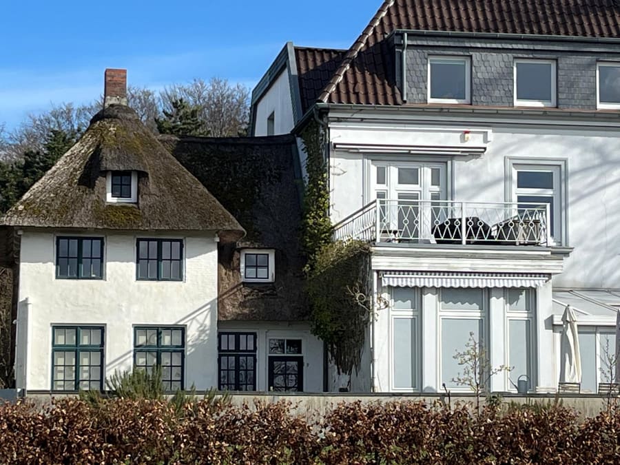 Altes reetgedecktes Haus mit Sprossenfenstern neben einer weißen Villa mit Balkon