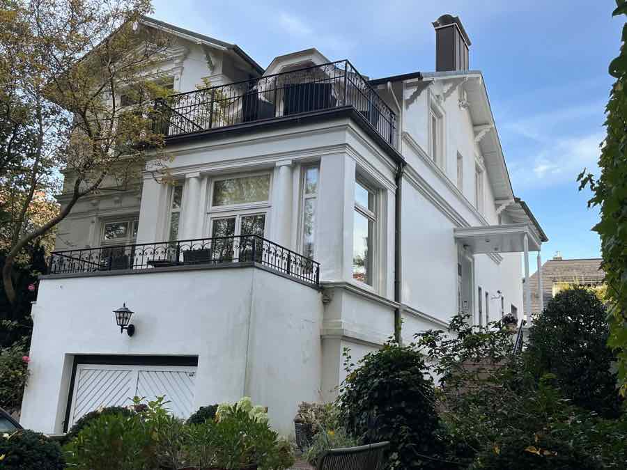 Weiße Villa mit schmiedeeisernen Balkonen, Garage und Garten vor blauem Himmel