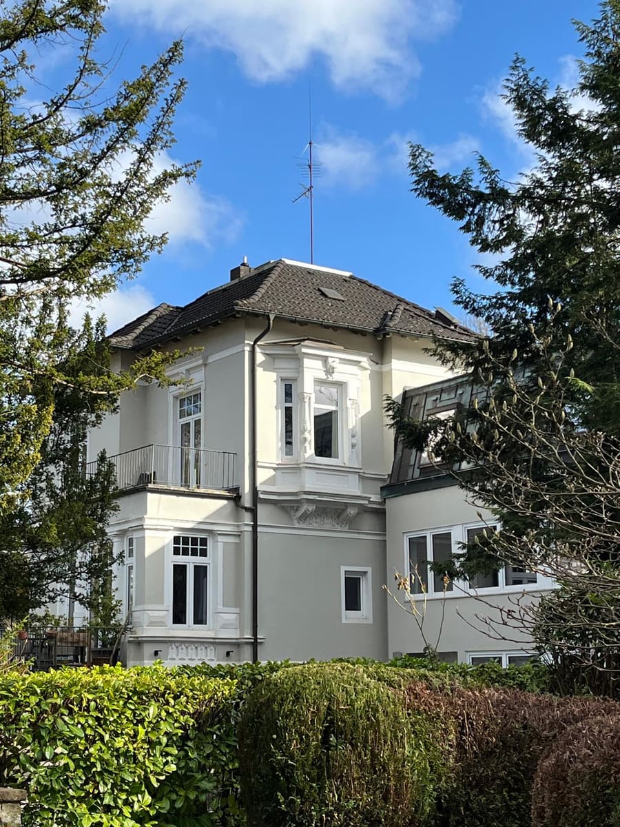 Helle Villa mit Erker und Walmdach zwischen Kiefern und Hecken